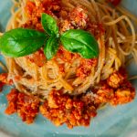 Vegane Bolognese mit Basilikum angerichtet auf einem blau-grünen Teller vor weißem Hintergrund.