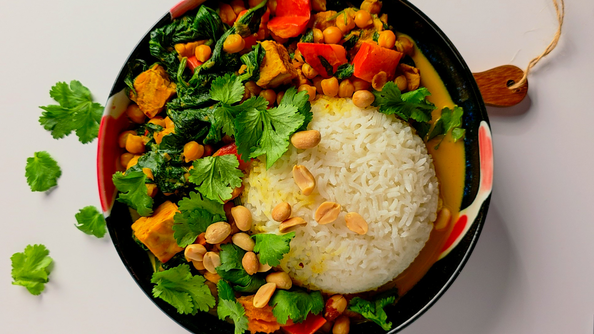 Bunte vegane Curry-Bowl mit weißem Reis, geröstetem Kürbis, Kichererbsen, Spinat, Paprika, Erdnüssen und Koriander.