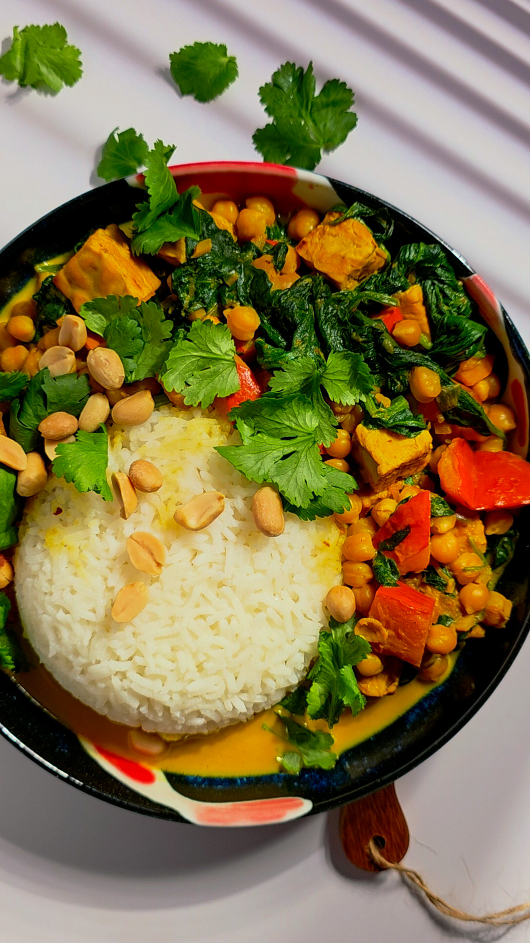 Veganes Curry mit Reis, Kürbis, Kichererbsen, Blattspinat, Erdnüssen und frischem Koriander in einer Schale.