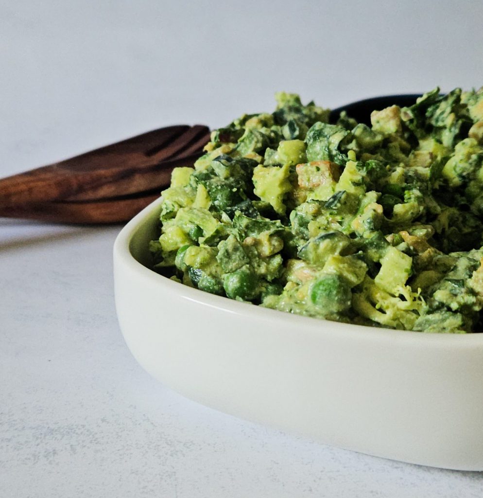 Grüner Salat mit Gurken, Erbsen, Tofu und weiteren Zutaten mit einem cremigen Dressing in einer Schüssel vor hölzernem Salatbesteck.