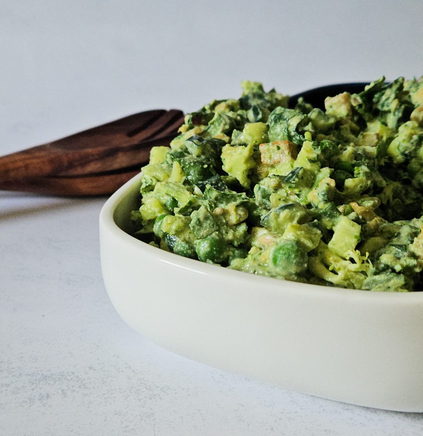 Grüner Salat mit Gurken, Erbsen, Tofu und weiteren Zutaten mit einem cremigen Dressing in einer Schüssel vor hölzernem Salatbesteck.
