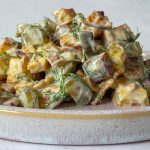 Seitlicher Blick auf Kartoffelsalat mit Tofu, Gurken, Zwiebeln und einem cremigen Dressing aus Joghurt und Dill.