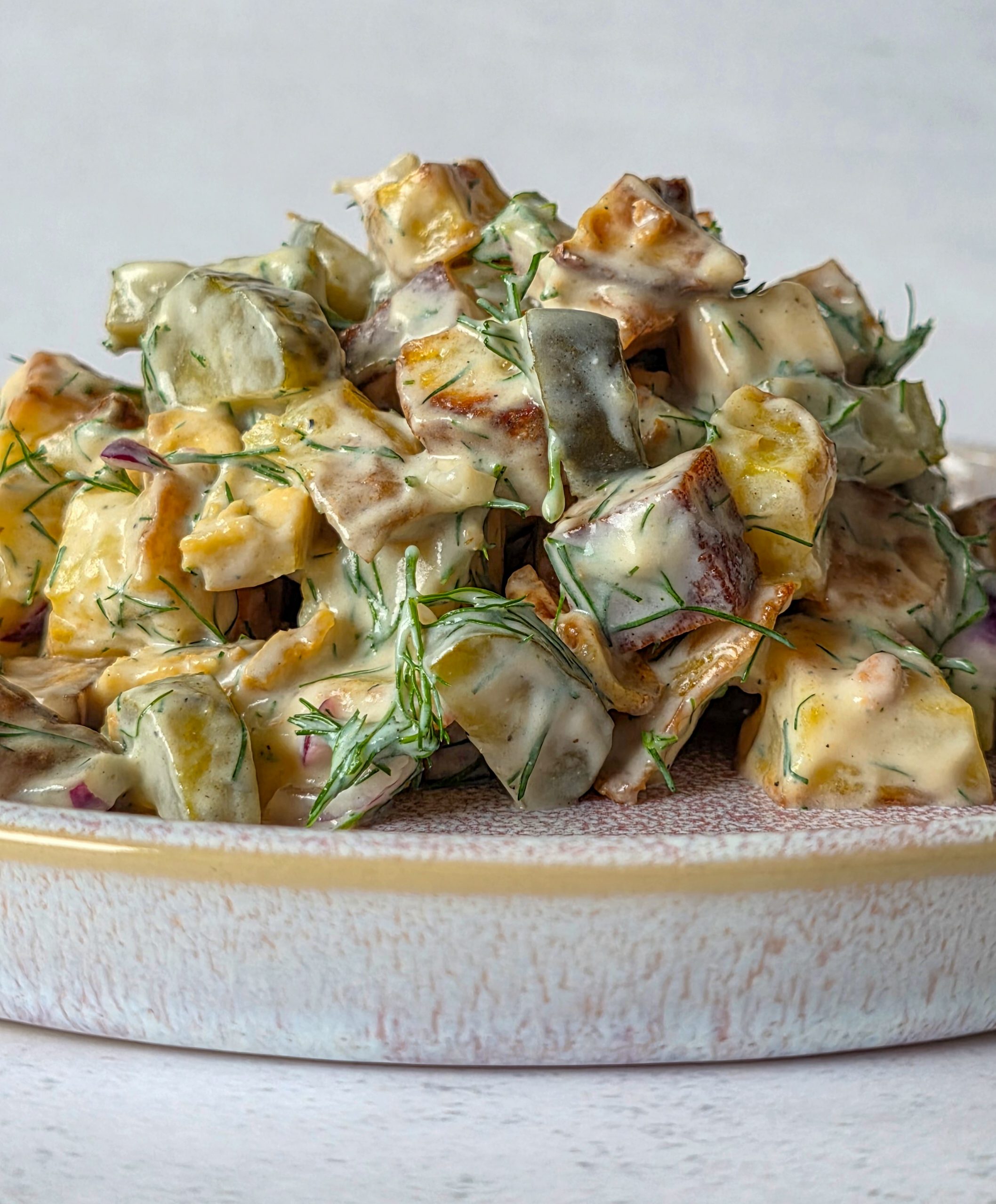 Seitlicher Blick auf Kartoffelsalat mit Tofu, Gurken, Zwiebeln und einem cremigen Dressing aus Joghurt und Dill.