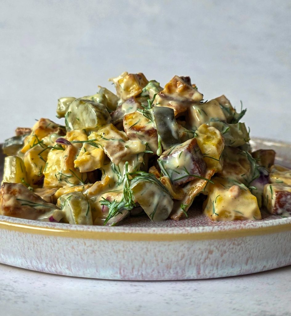 Seitlicher Blick auf Kartoffelsalat mit Tofu, Gurken, Zwiebeln und einem cremigen Dressing aus Joghurt und Dill.