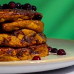 Fluffige vegane Pancakes mit Schokostückchen, auf einem hellen Teller serviert, vor leuchtend grünem Hintergrund.