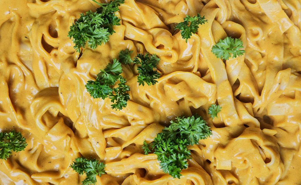 Bandnudeln in einer leuchtend gelben, cremigen Currysauce, dekoriert mit grüner Petersilie.