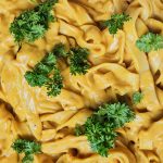Bandnudeln in einer leuchtend gelben, cremigen Currysauce, dekoriert mit grüner Petersilie.