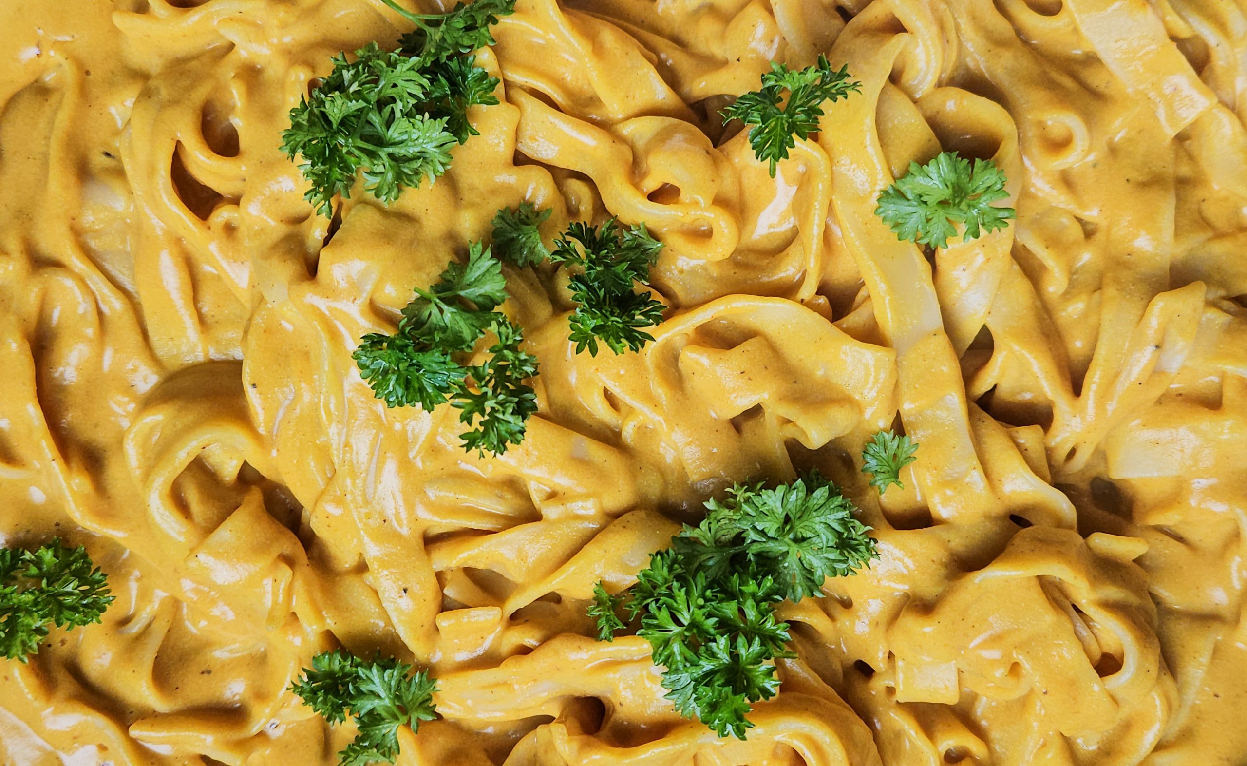 Bandnudeln in einer leuchtend gelben, cremigen Currysauce, dekoriert mit grüner Petersilie.
