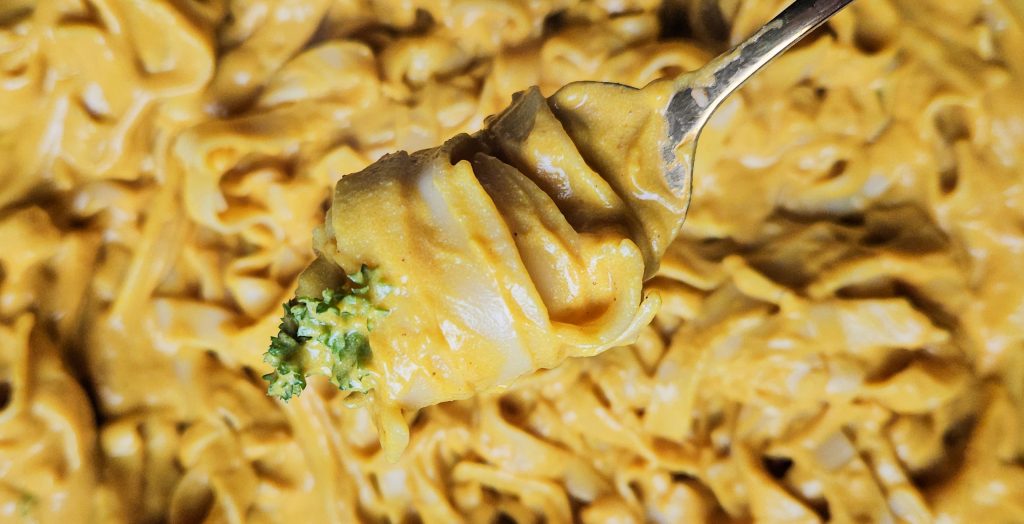 Vegane Kürbis Pasta in Nahaufnahme in sämiger gelber Sauce auf einer Gabel aufgerollt, mit frischen Petersilienblättern als Topping.