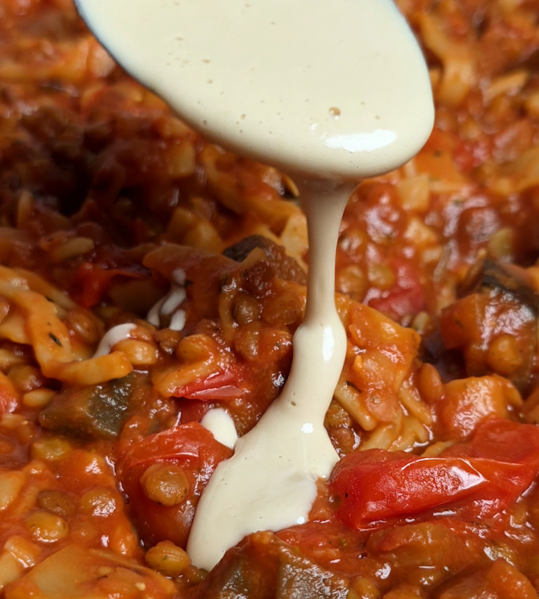 Weiße, cremige Sauce wird von einem Löffel auf die vegane Lasagnesuppe gegeben.