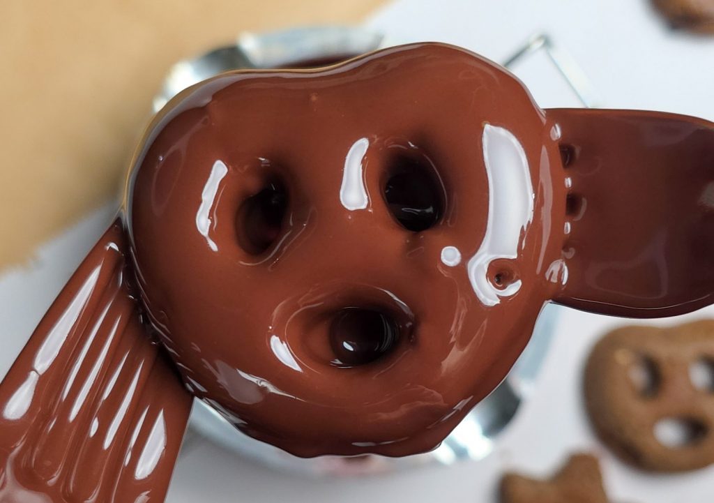 Veganes Lebkuchen-Gebäck in Brezel-Form wird mit flüssiger, glänzender Schokolade überzogen.