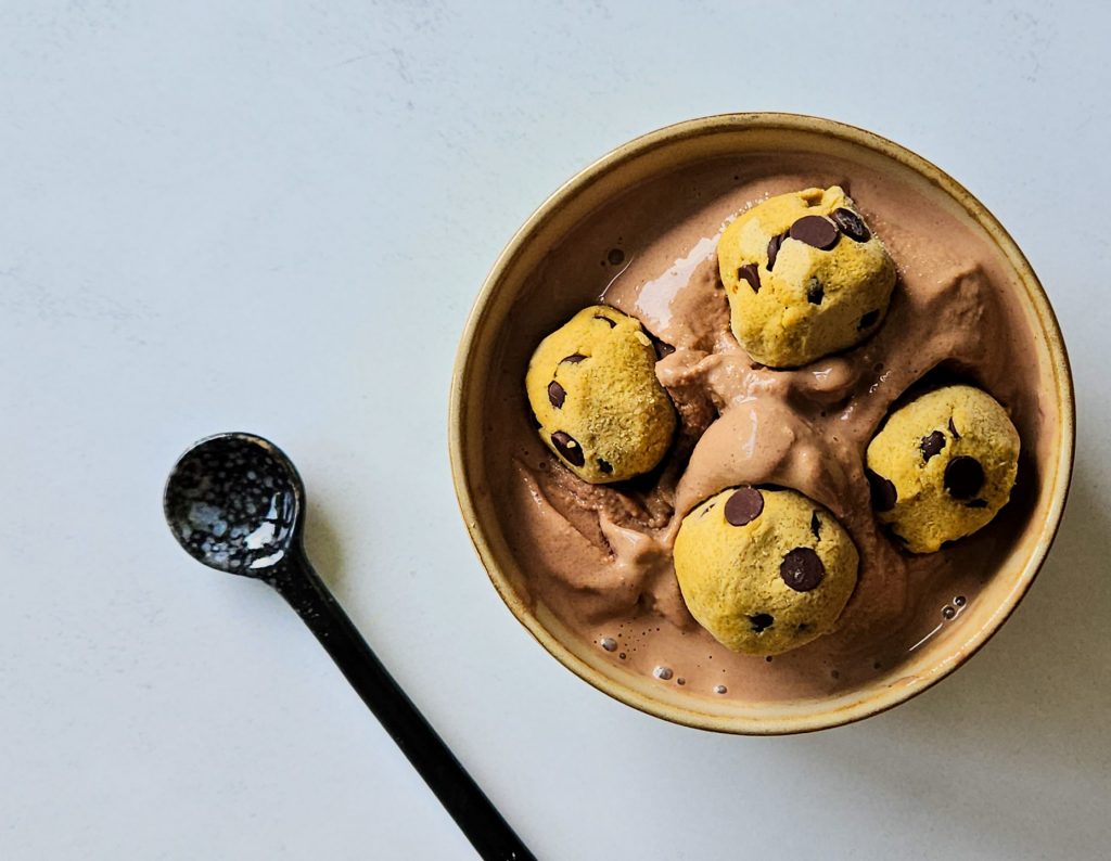 Schokoeis mit vier Cookie Dough Bällchen in einer Schüssel, daneben ein schwarzer Löffel.