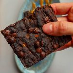 Nahaufnahme eines proteinreichen veganen Zucchini-Brownies mit Schokodrops, von Hand gehalten.