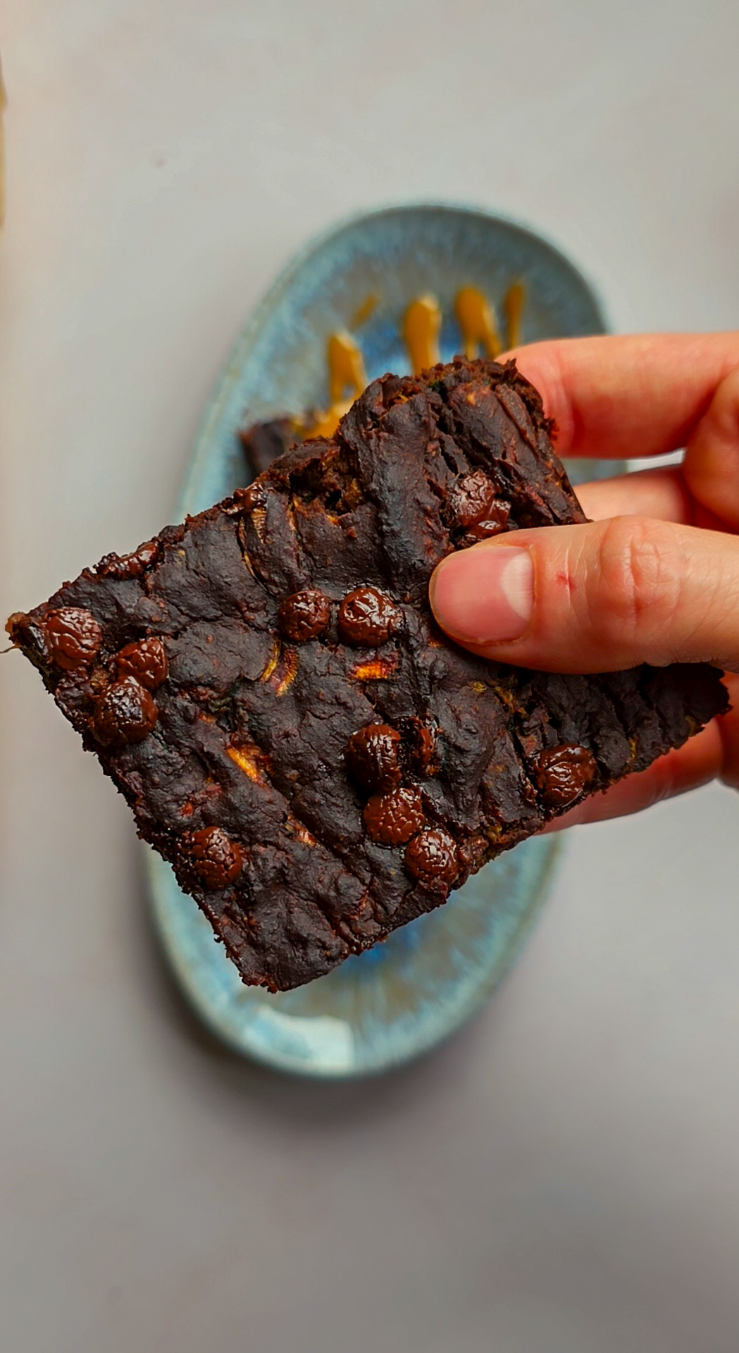 Nahaufnahme eines proteinreichen veganen Zucchini-Brownies mit Schokodrops, von Hand gehalten.