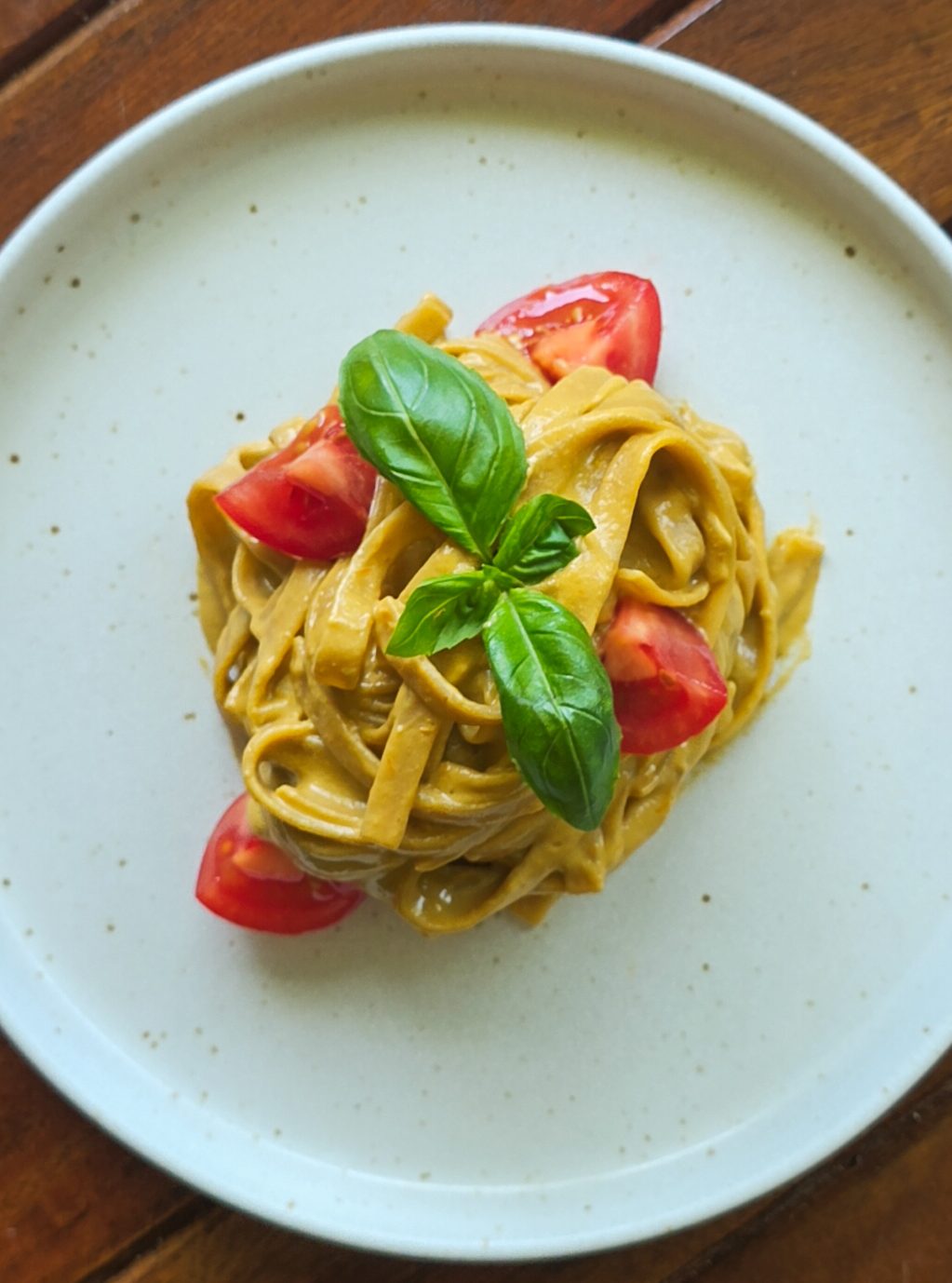 Tagliatelle mit veganer Ricotta Tomaten Sauce auf einem beigen Teller, verziert mit Tomaten und Basilikum.