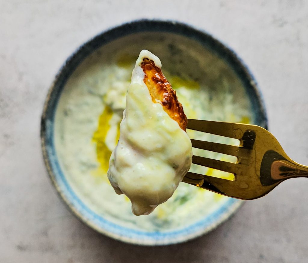 Nahaufnahme veganer Tzatziki: Ein Stück Kartoffel getunkt in cremigen veganen Tzatziki mit Olivenöl.