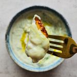 Nahaufnahme veganer Tzatziki: Ein Stück Kartoffel getunkt in cremigen veganen Tzatziki mit Olivenöl.