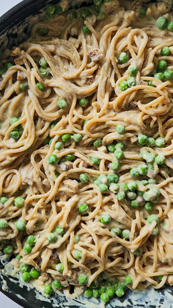 Spaghetti in einer Pfanne vermischt mit einer cremigen hellen Soße, grünen Erbsen und kleinen Tofuwürfeln