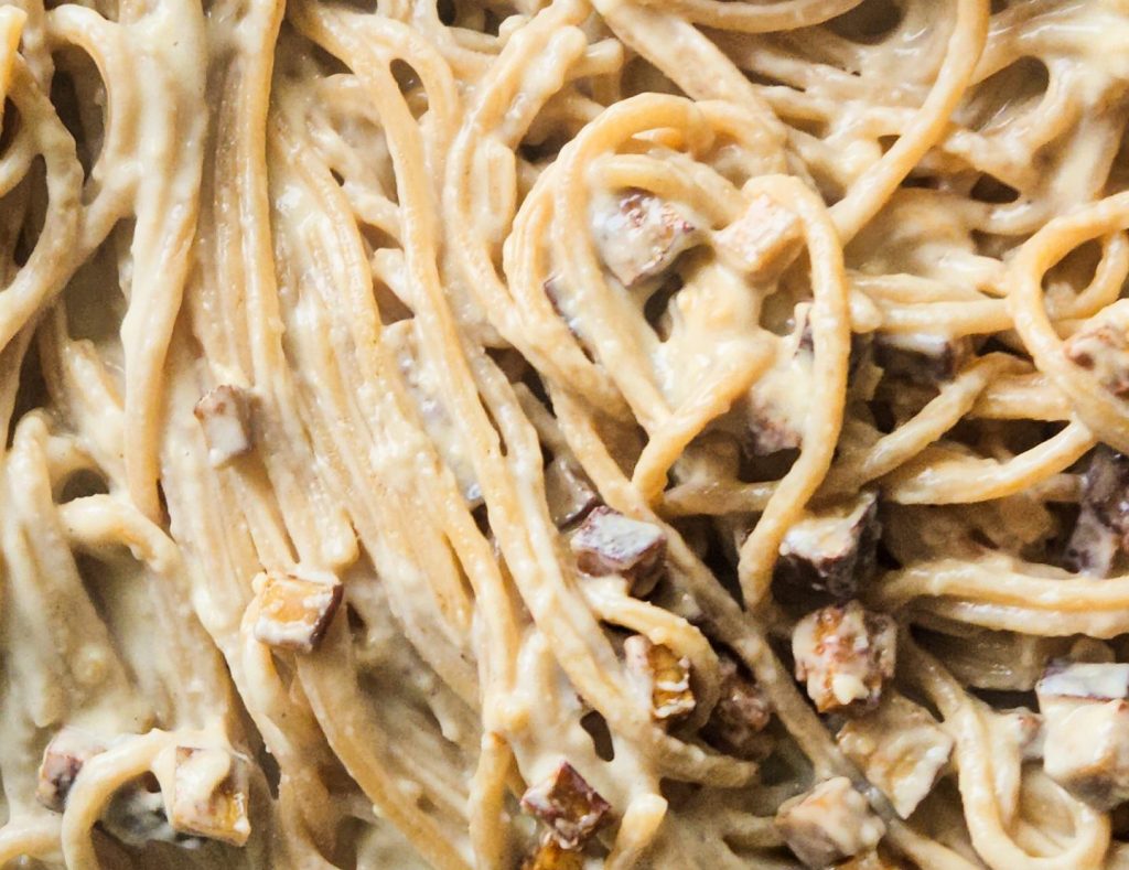 Nahaufnahme von Spaghetti in einer Pfanne vermischt mit einer cremigen hellen Soße und kleinen Tofuwürfeln