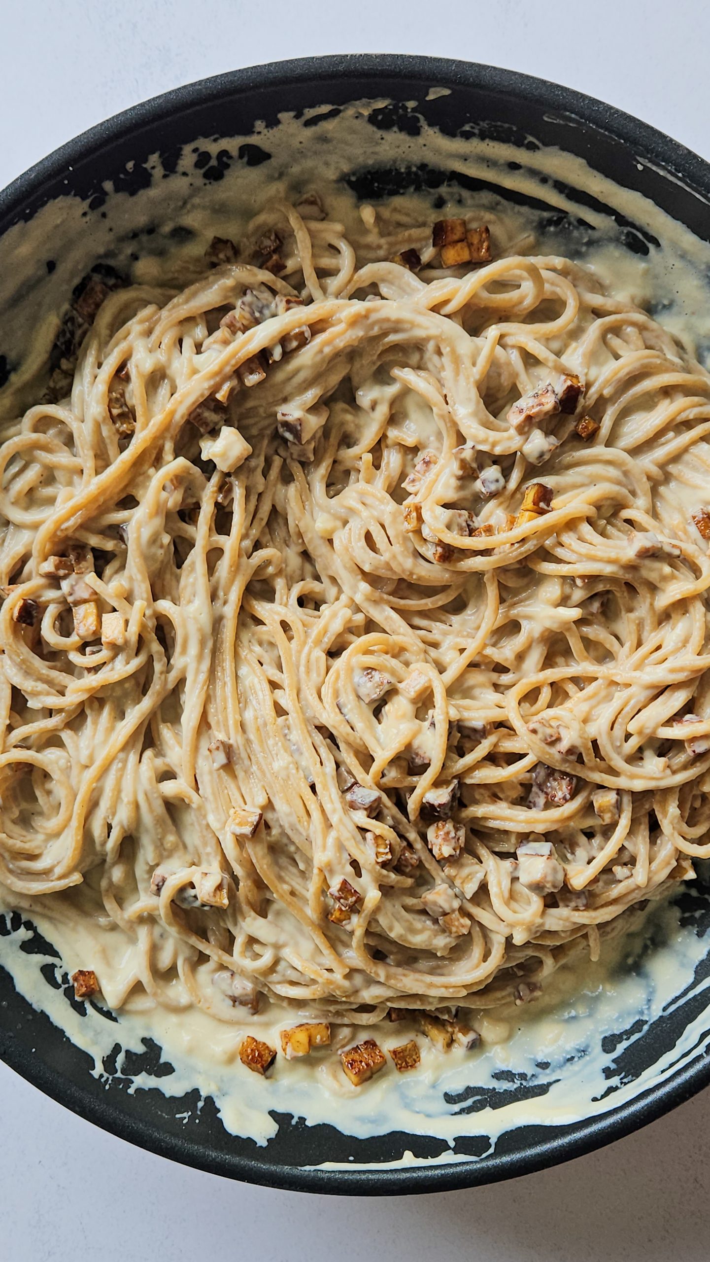 Spaghetti in einer Pfanne vermischt mit einer cremigen hellen Soße und kleinen Tofuwürfeln