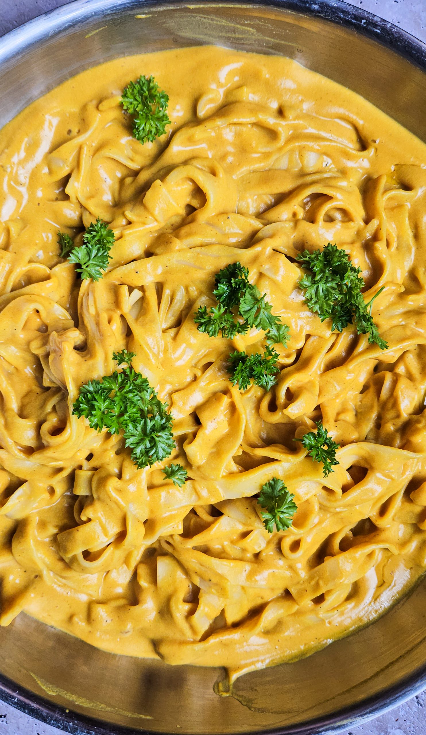 Cremige vegane Pasta mit goldgelber Sauce, verfeinert mit frischer Petersilie als Garnitur.