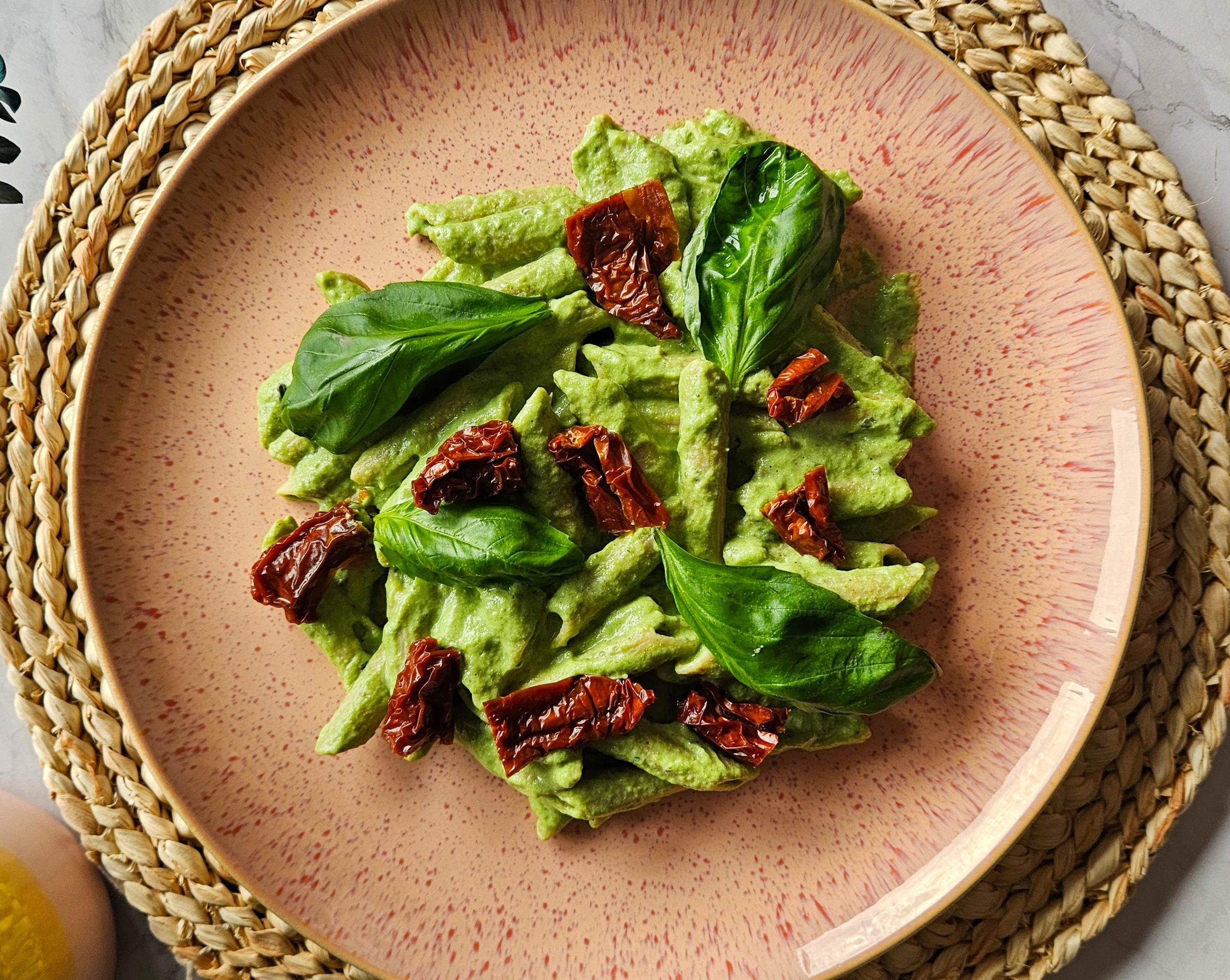 Pasta mit einer cremigen grünen Soße verziert mit Basilikum und getrockneten Tomaten auf einem rosafarbenen Teller