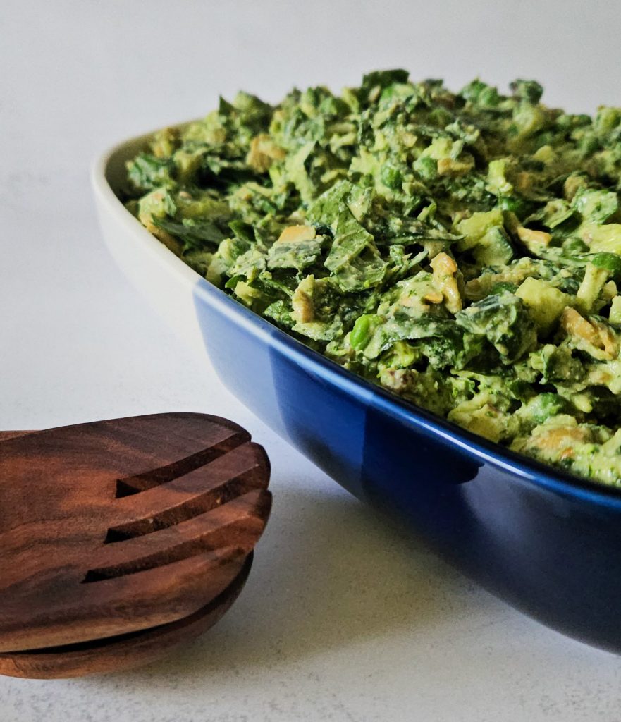 Grüner Salat mit Gurken, Erbsen, Tofu und weiteren Zutaten mit einem cremigen Dressing in einer Schüssel neben hölzernem Salatbesteck.