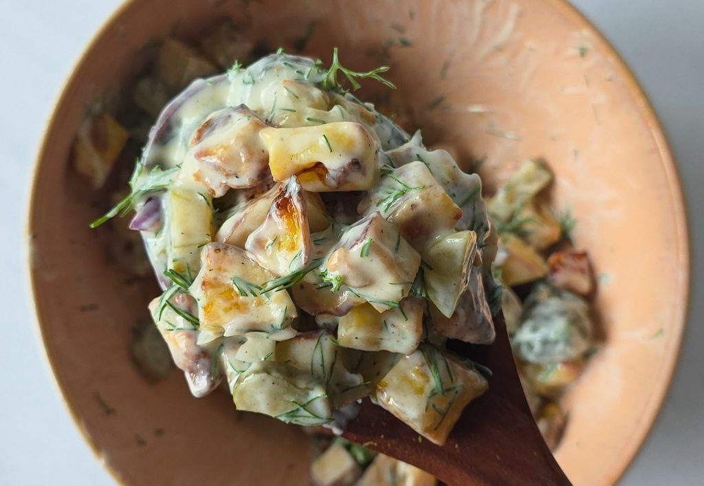 Kartoffelsalat mit Tofu, Gurken, Zwiebeln und einem cremigen Dressing aus Joghurt und Dill auf einem großen Holzlöffel.