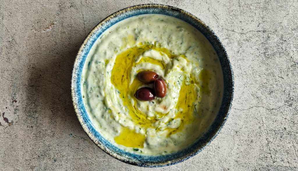 Frisch angerichteter veganer Tzatziki in einer Schüssel, verfeinert mit Oliven und Olivenöl, ideal als gesunder veganer Dip.
