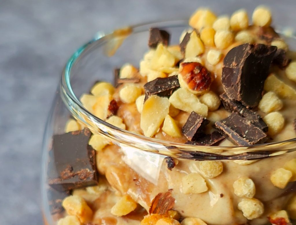 Cremiges Haselnuss-Vanille-Eis mit Dattelkaramell getoppt mit Haselnüssen, Zartbitterschokolade und Sojacrispies. Veganes Eis selber machen.
