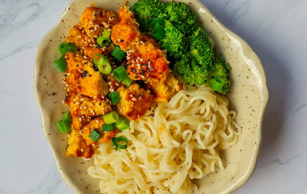 Einfach Tofu zubereiten. Auf einem Teller angerichteter knuspriger Tofu mit Sesam und Frühlingszwiebeln bestreut, daneben Brokkoli und Mie-Nudeln.